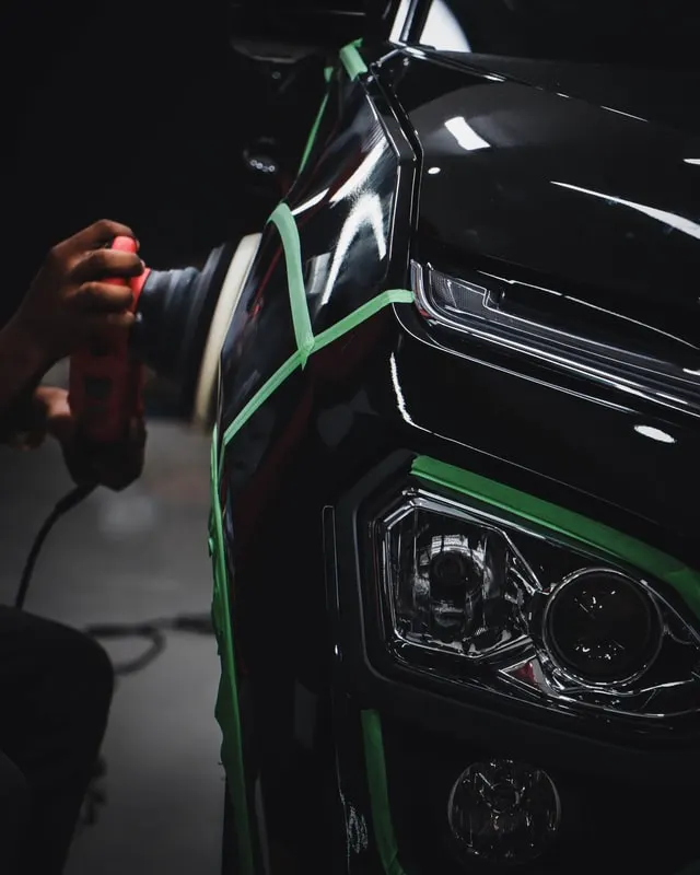 Technician polishing black vehicle paint beside a protected headlight